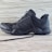 A black athletic shoe with a rugged sole and mesh detailing, designed for outdoor activities. It features brand markings on the side and is positioned against a light wooden background.