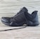 A black athletic shoe with a rugged sole and mesh detailing, designed for outdoor activities. It features brand markings on the side and is positioned against a light wooden background.