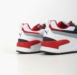 Two athletic shoes with bold red, white, and dark blue color blocking. The shoes feature a sleek, modern design with a flat sole and a recognizable logo in black on the heel. The upper part is made of a mix of textiles with some parts having perforations for breathability.