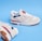 A pair of beige athletic shoes with white laces and blue and red accents. The shoes feature a noticeable logo on the side and are set against a solid blue background.